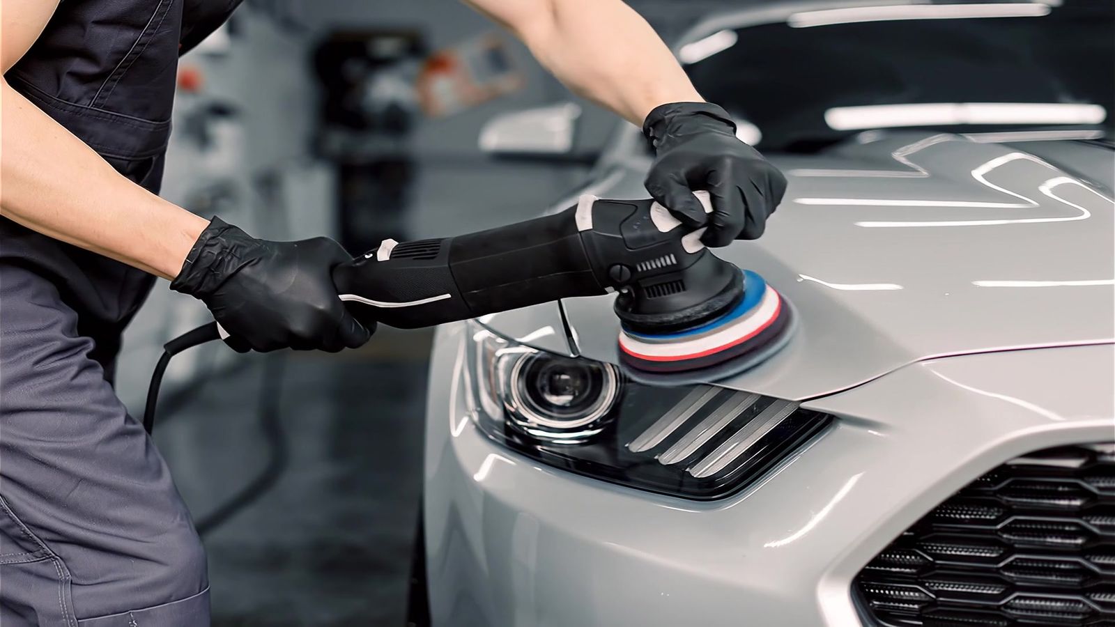 Medewerker polijst de motorkap van een zilvergrijze auto met een polijstmachine