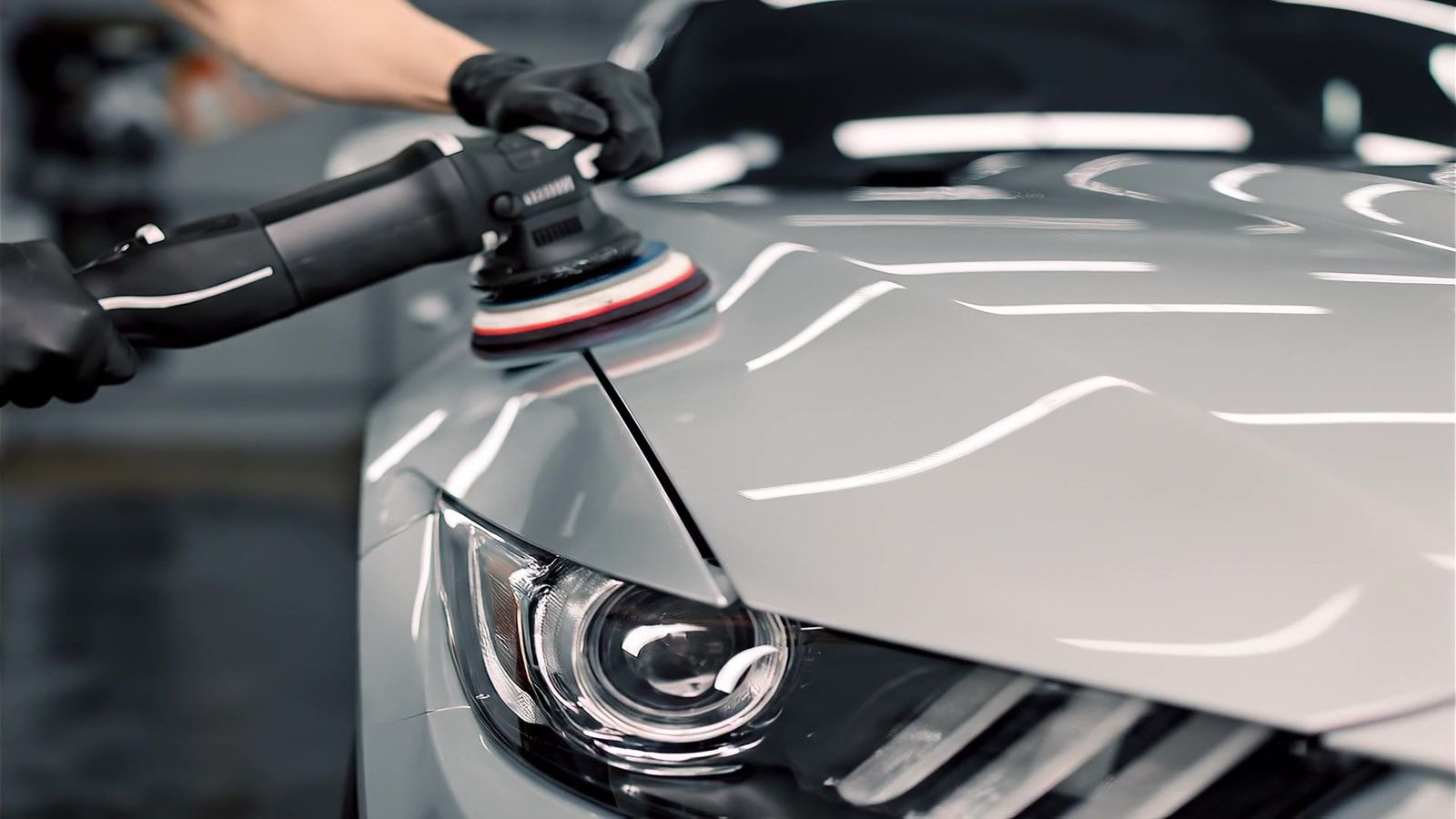Polijstmachine bij de koplamp van een zilvergrijze auto